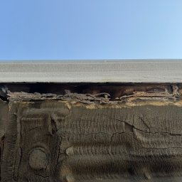 Maciej Grzęda MG Serwis - Silnie skorodowany fragment podwozia samochodu, widoczne liczne ogniska rdzy i uszkodzenia metalu, na tle błękitnego nieba.