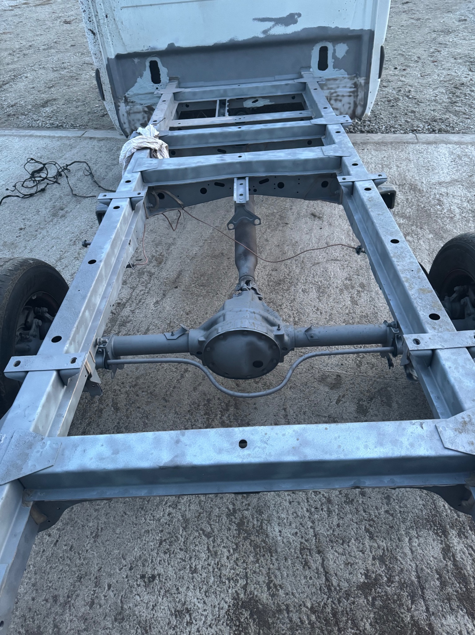 Oczyszczona i pomalowana rama samochodu z widocznym tylnym mostem, stojąca na betonowym podłożu, widoczne ślady szpachli na karoserii.