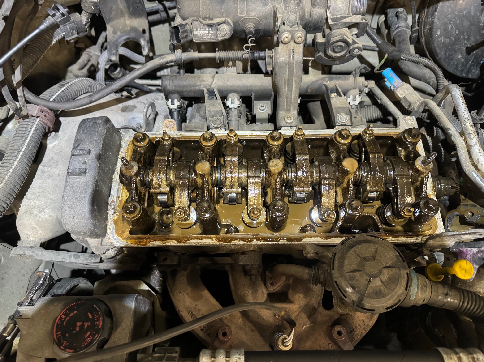 Otwarty silnik samochodowy, widoczne elementy głowicy cylindrów pokryte olejem, w tle inne komponenty silnika.