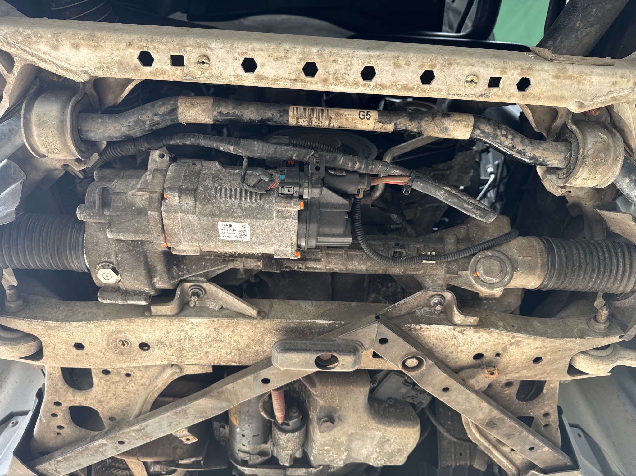 Widok podwozia samochodu marki BMW z widocznym układem kierowniczym, elementami zawieszenia i przewodami. Ujęcie od dołu, oświetlenie naturalne.