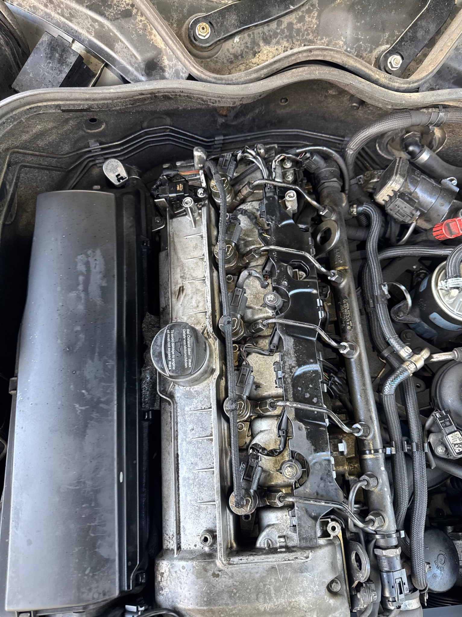 Silnik samochodu z widocznymi przewodami, wtryskiwaczami i elementami osprzętu. Widoczne ślady użytkowania i potencjalne zabrudzenia.