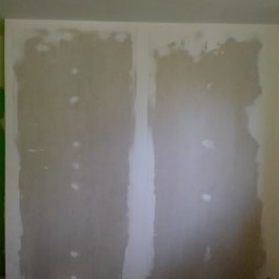 Krzysztof Wójcicki - Przygotowana do tapetowania ściana z widocznymi śladami szpachlowania, zabezpieczona folią malarską na podłodze, z widocznymi puszkami elektrycznymi.