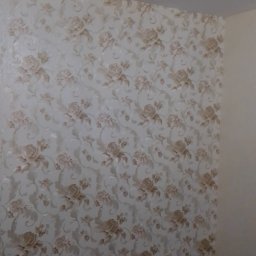 Krzysztof Wójcicki - Ściana po tapetowaniu z beżowymi kwiatami, widoczne puszki z klejem i narzędzia malarskie na czarnej folii ochronnej.