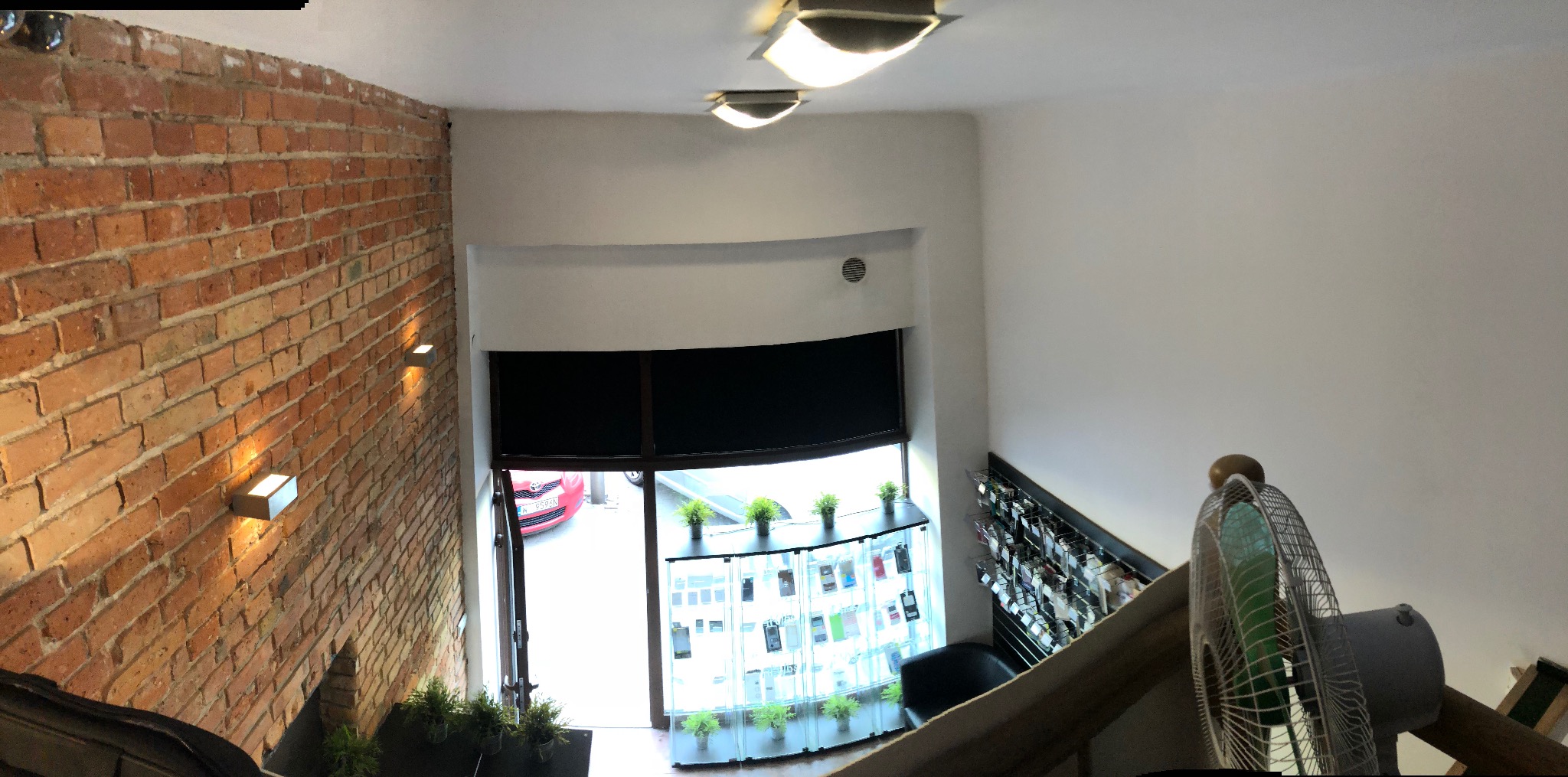 Wnętrze biura z ceglaną ścianą, oknem wystawowym z ekspozycją telefonów i wentylatorem na pierwszym planie, widok z góry