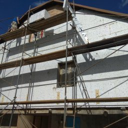 Bodzio - Ocieplanie elewacji domu jednorodzinnego z użyciem styropianu, widoczne rusztowanie i pracownicy na wysokości.