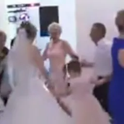 Para młoda w trakcie pierwszego tańca na weselu, otoczona gośćmi, w tle widoczny kolumnowy element dekoracyjny i oświetlenie sceniczne.