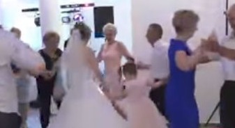 Para młoda w trakcie pierwszego tańca na weselu, otoczona gośćmi, w tle widoczny kolumnowy element dekoracyjny i oświetlenie sceniczne.