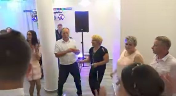 Grupa osób tańczy na parkiecie podczas imprezy, widoczne oświetlenie dyskotekowe i głośnik na statywie.