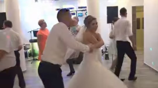 Para młoda tańczy na weselu, w tle widoczni goście i elementy sceny z oświetleniem.