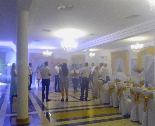 Sala bankietowa z gośćmi w trakcie przyjęcia, widoczne stoły z dekoracjami i oświetlenie dekoracyjne.