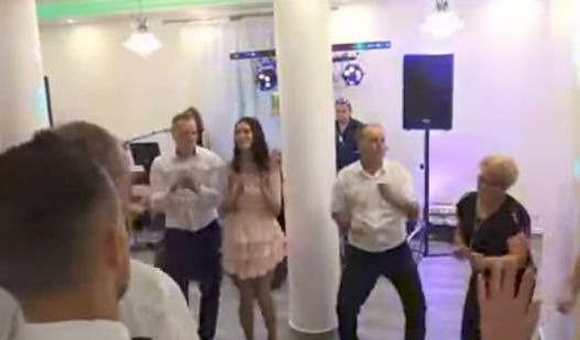 Tańczący goście weselni w sali z kolumną, nagłośnieniem i oświetleniem w tle.