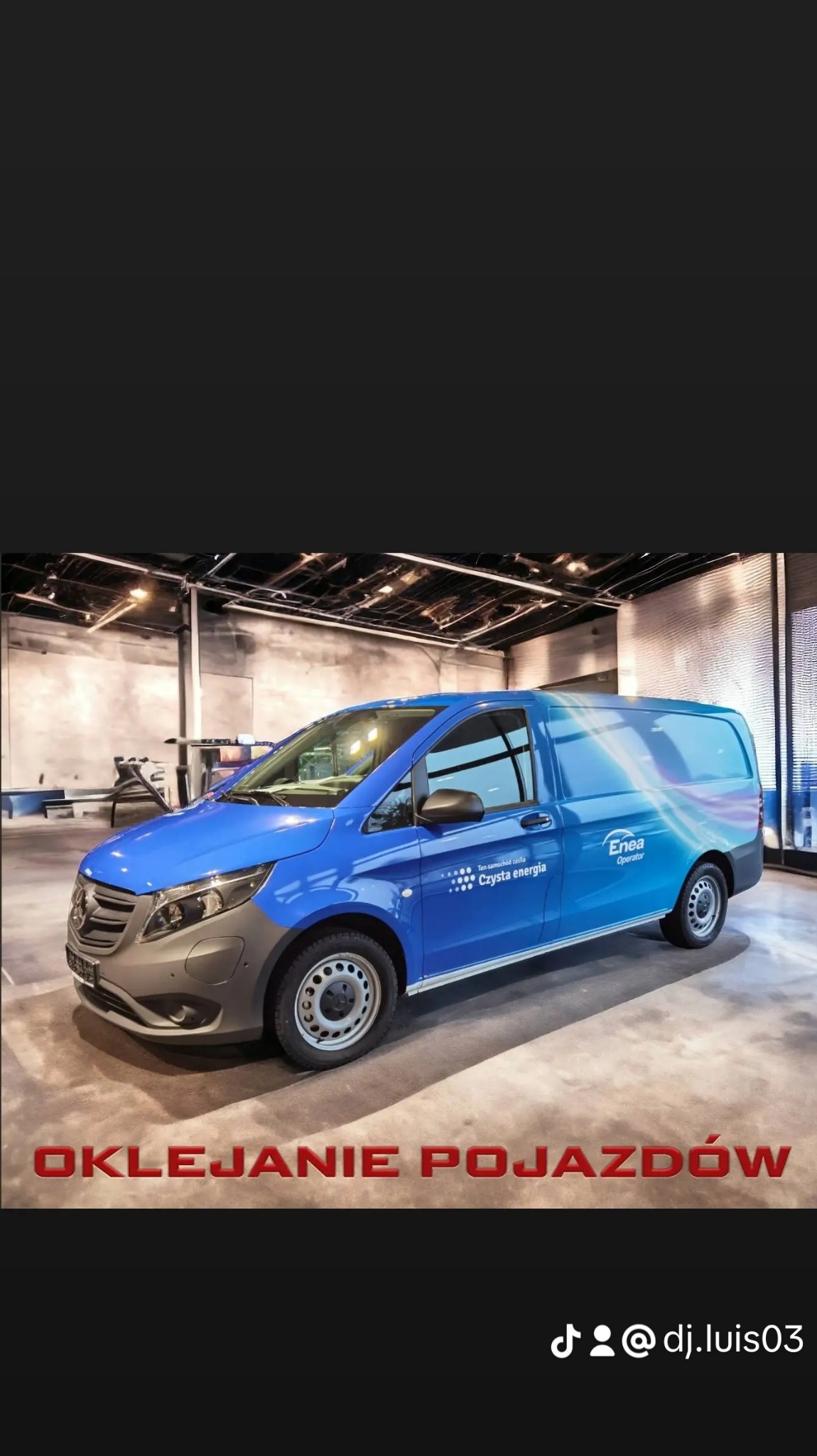 Niebieski samochód dostawczy marki Mercedes-Benz z oklejeniem reklamowym firmy Enea Operator, prezentowany w nowoczesnym wnętrzu hali.