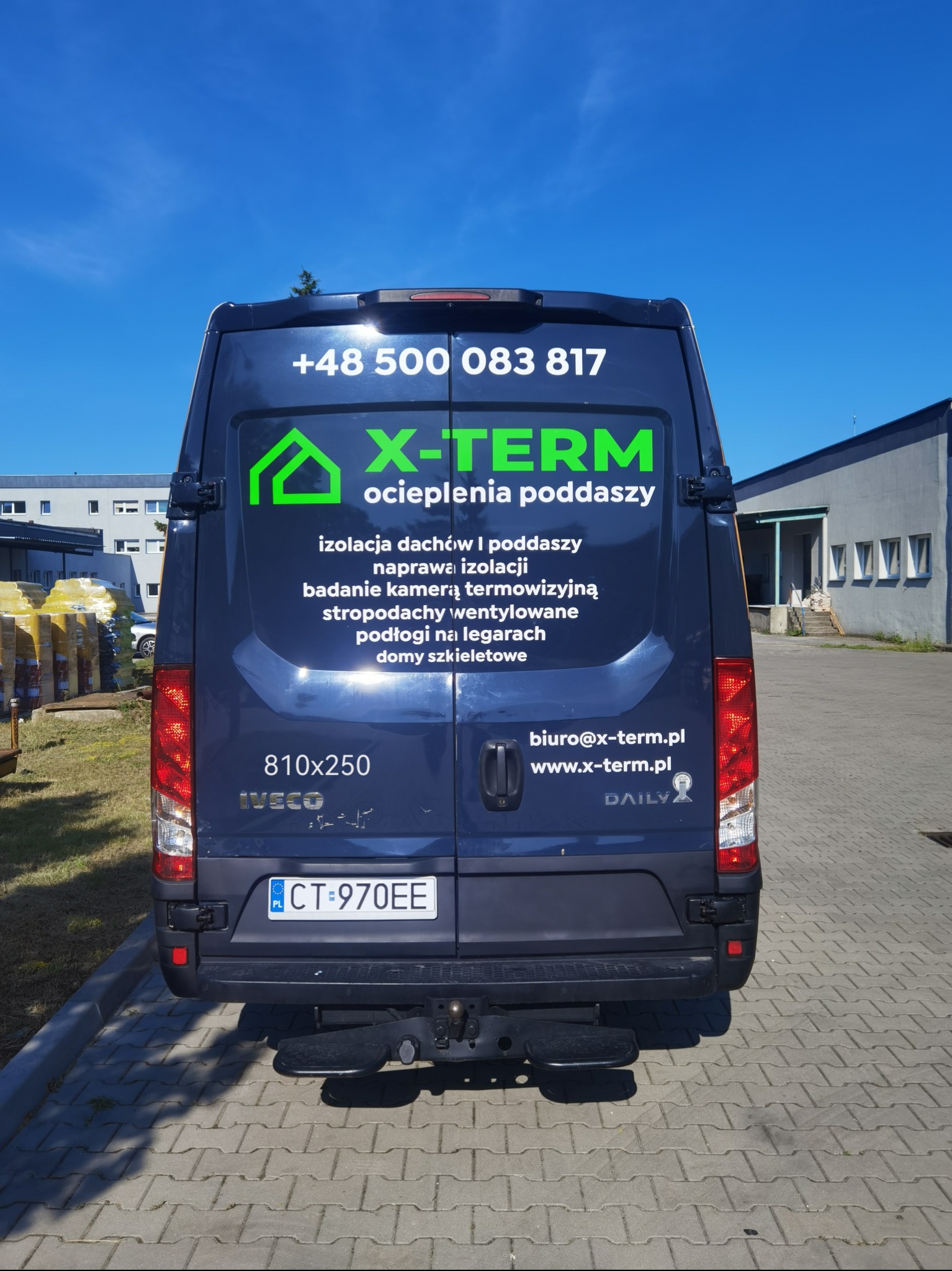 Granatowy bus z reklamą firmy X-TERM, specjalizującej się w ociepleniach poddaszy. Widoczne dane kontaktowe i zakres usług. Tablica rejestracyjna CT 970EE.