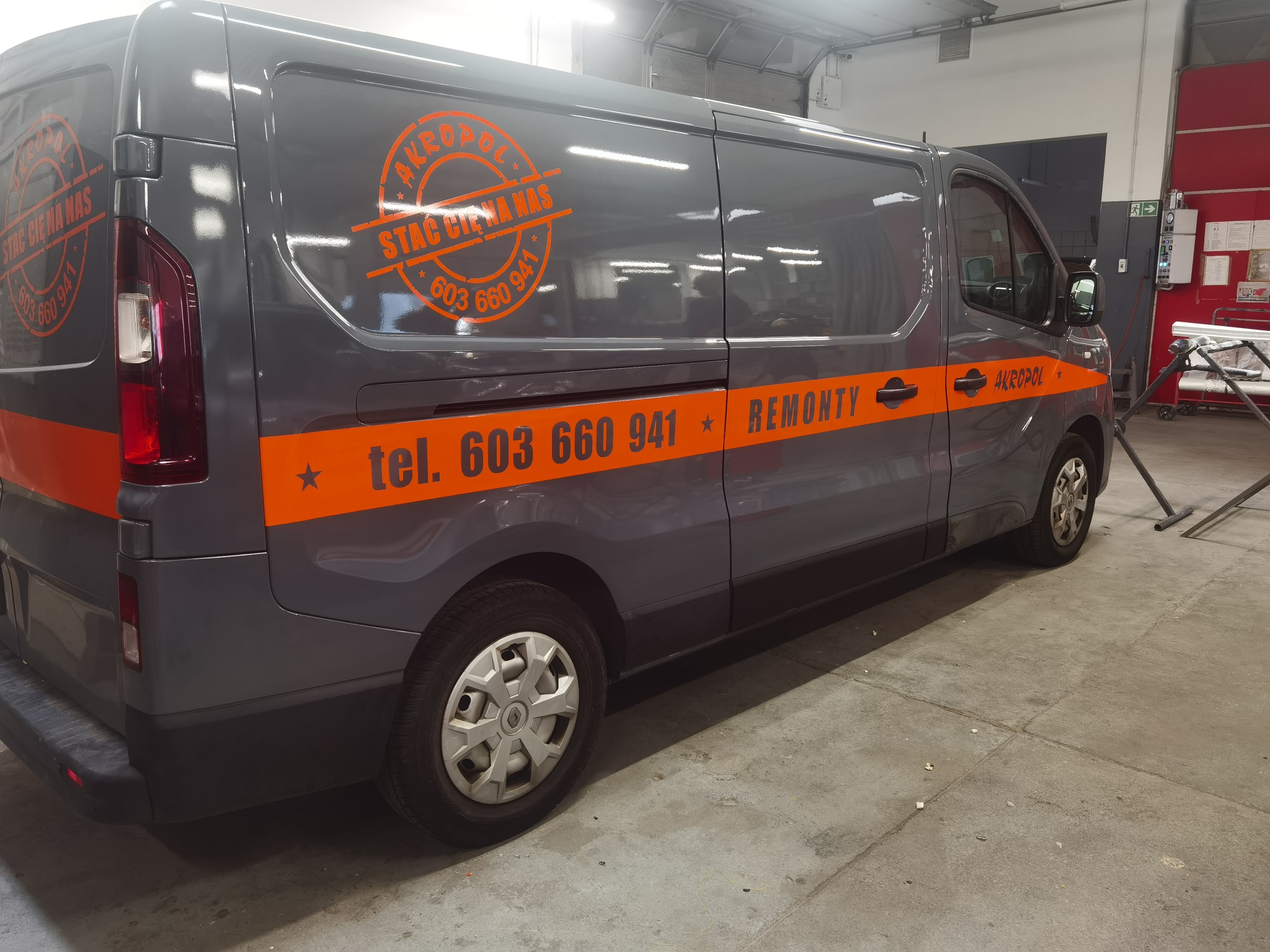 Szary bus z pomarańczową grafiką firmy remontowej: logo 'Akropol', hasło 'Stać Cię na Nas' i numer tel. 603 660 941. Prezentacja oklejania pojazdu.