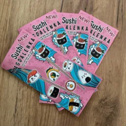 Stos różowych ulotek reklamowych sushi z rysunkowymi ilustracjami i danymi kontaktowymi na drewnianym tle.