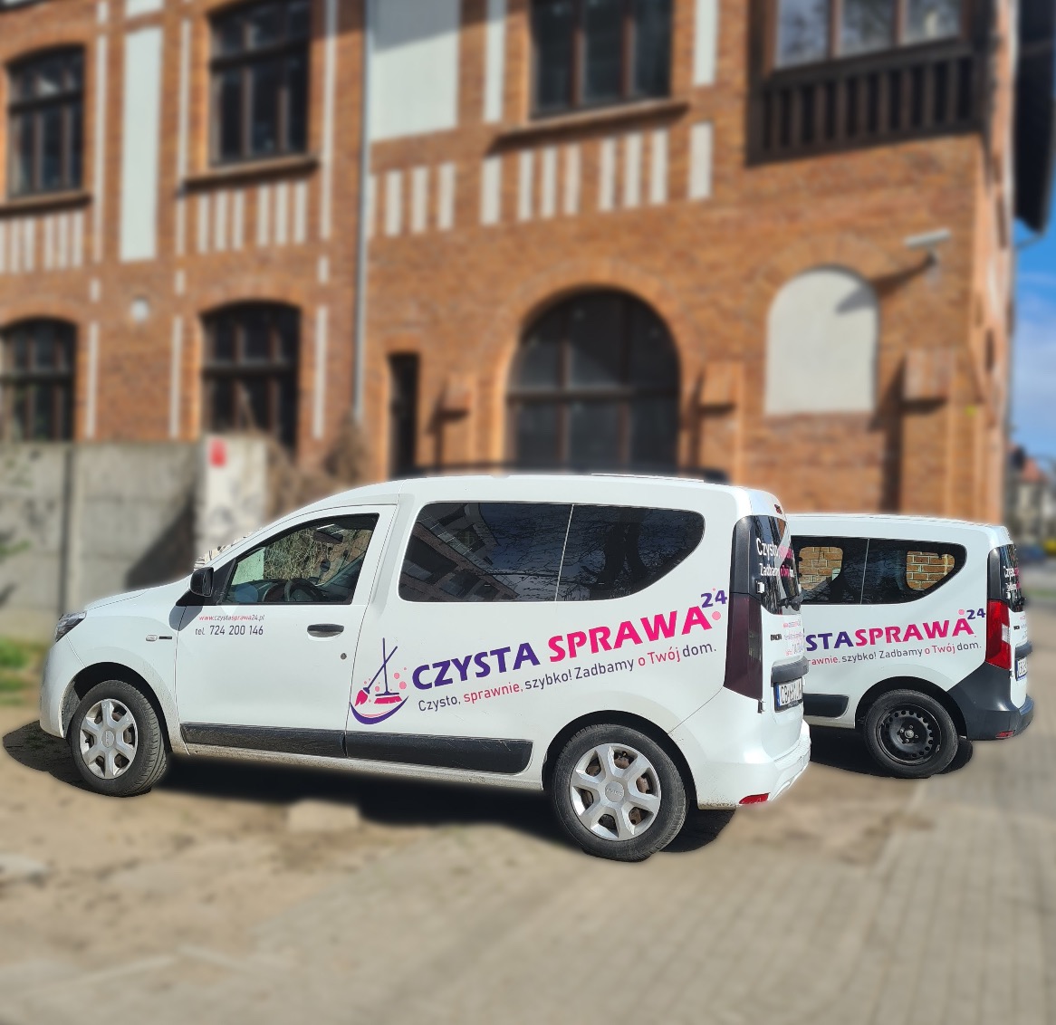 Dwa białe samochody dostawcze z logo firmy sprzątającej 'Czysta Sprawa' zaparkowane przed budynkiem z czerwonej cegły.