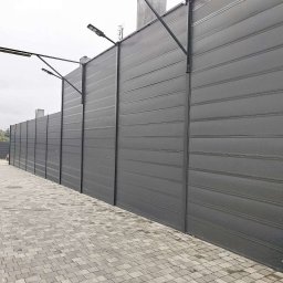 ROSMARIN Sp. z o.o. - Długie, szare ogrodzenie panelowe z oświetleniem LED wzdłuż chodnika z kostki brukowej, widok z perspektywy przechodnia.