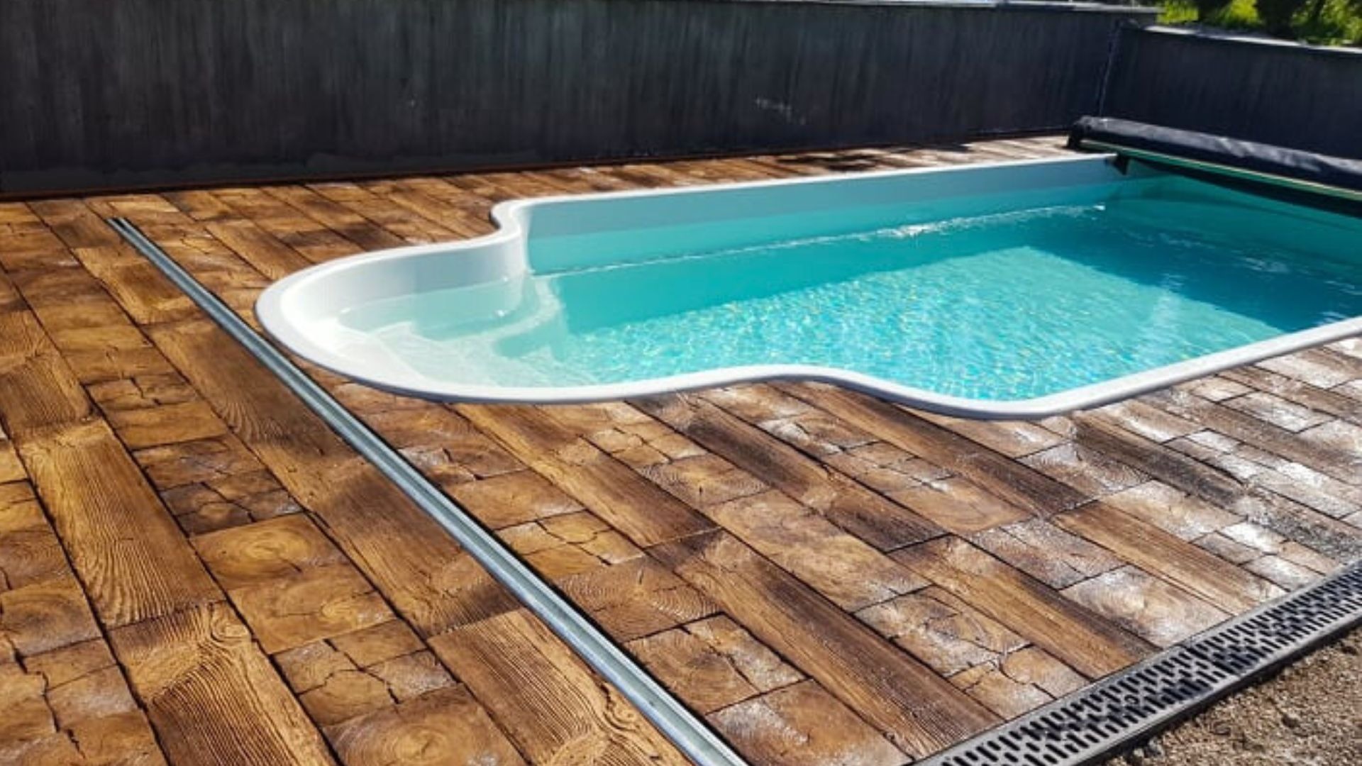 Basen z turkusową wodą otoczony betonową podłogą imitującą drewniane deski, widoczne odpływy liniowe.