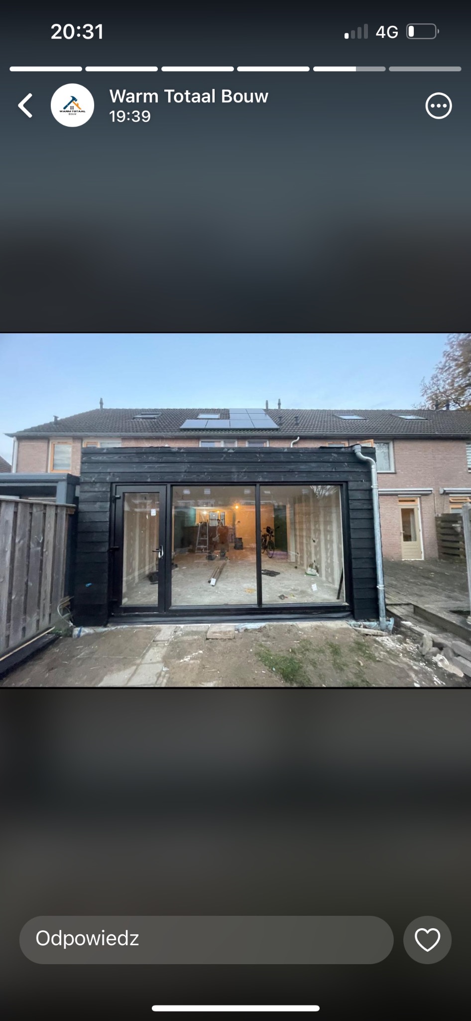 Dobudówka do domu z dużym oknem i czarną elewacją drewnianą, widoczne wnętrze w trakcie prac wykończeniowych, drabina i rower w środku.