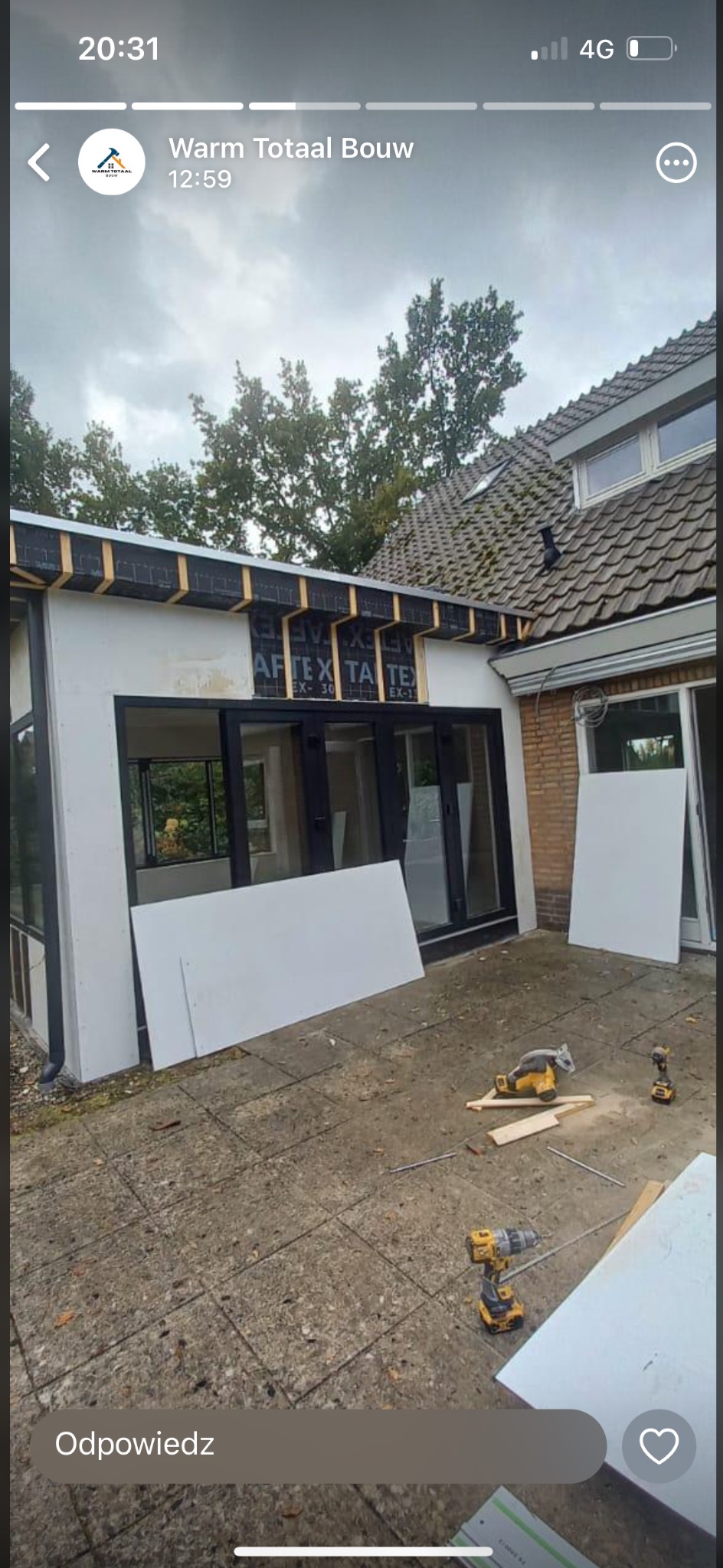 Rozbudowa domu w trakcie realizacji: widoczne elementy konstrukcyjne, czarne ramy okienne, płyty izolacyjne i narzędzia na zewnątrz budynku.