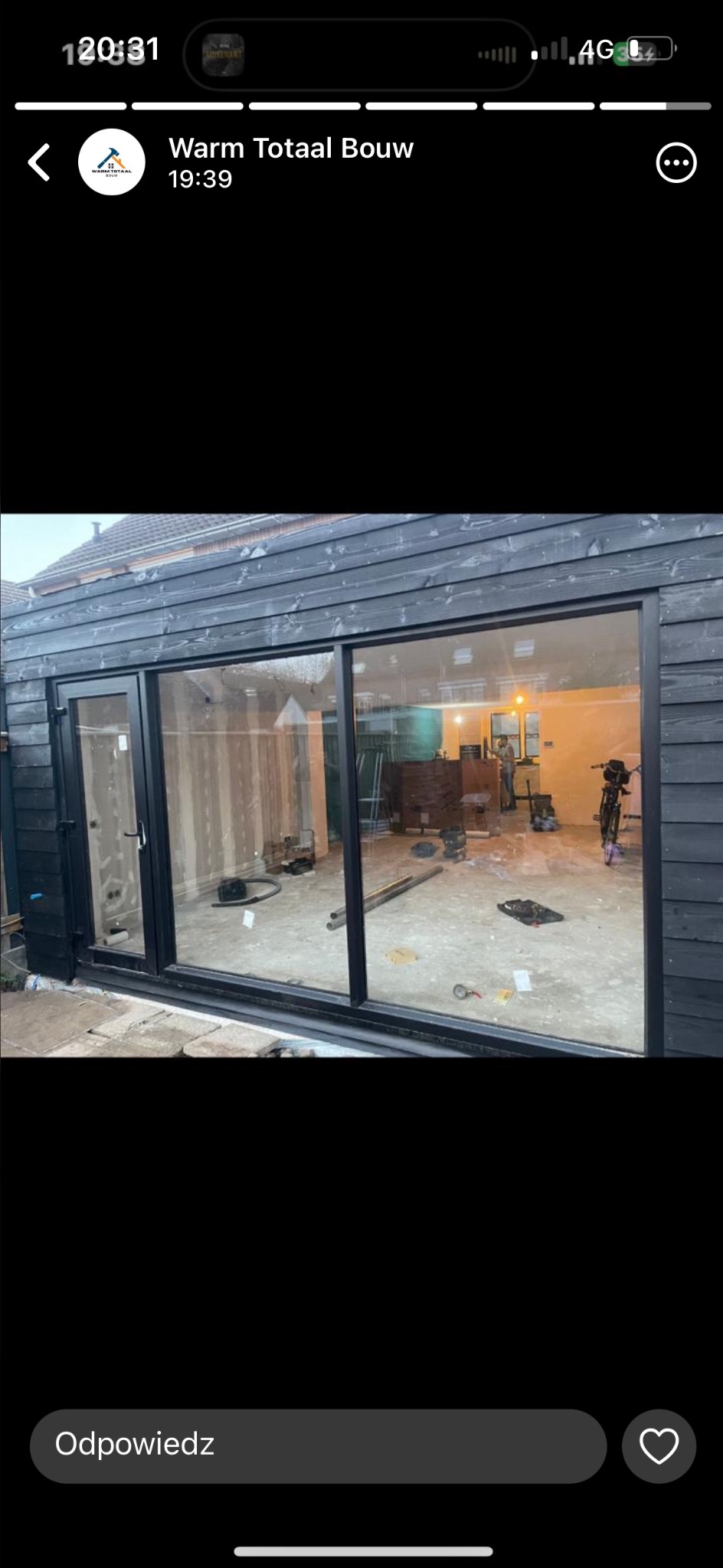 Dobudówka do domu z dużymi przesuwnymi oknami w czarnych ramach, widok na surowy stan wnętrza z widocznymi instalacjami i narzędziami.