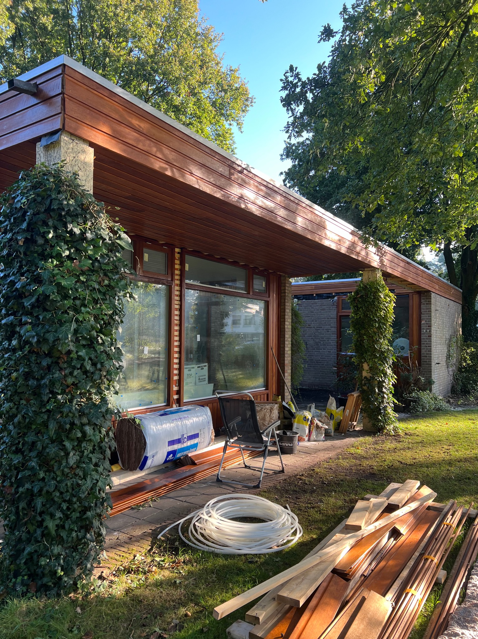 Budynek z płaskim dachem i drewnianą elewacją w trakcie rozbudowy, widoczne materiały budowlane, ocieplenie i narzędzia na zewnątrz.