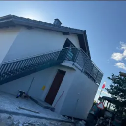 Metalowe schody zewnętrzne z balustradą prowadzące na balkon domu jednorodzinnego w trakcie wykańczania. Widoczny ciągnik i narzędzia.