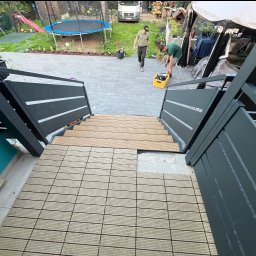 KRYCMET YEVHEN CHEKERLAN - Montaż drewnianej podłogi tarasowej na schodach z metalową balustradą w ogrodzie. Widoczny etap prac, narzędzia i osoby w tle. Kąt ujęcia z góry.