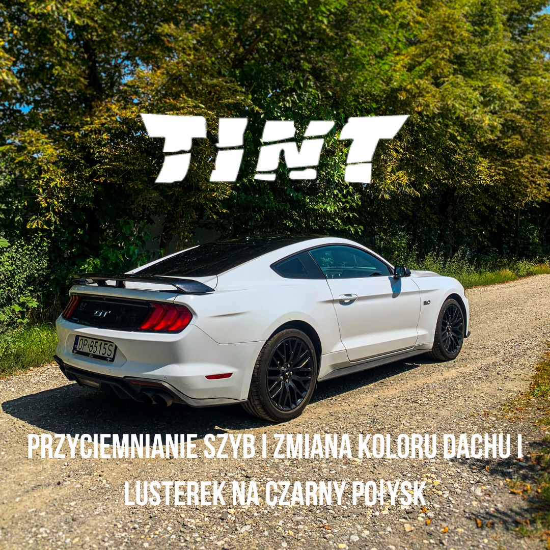 Biały Ford Mustang z przyciemnionymi szybami i czarnym dachem, stojący na żwirowej drodze, z widocznym napisem 'TINT' na górze zdjęcia.