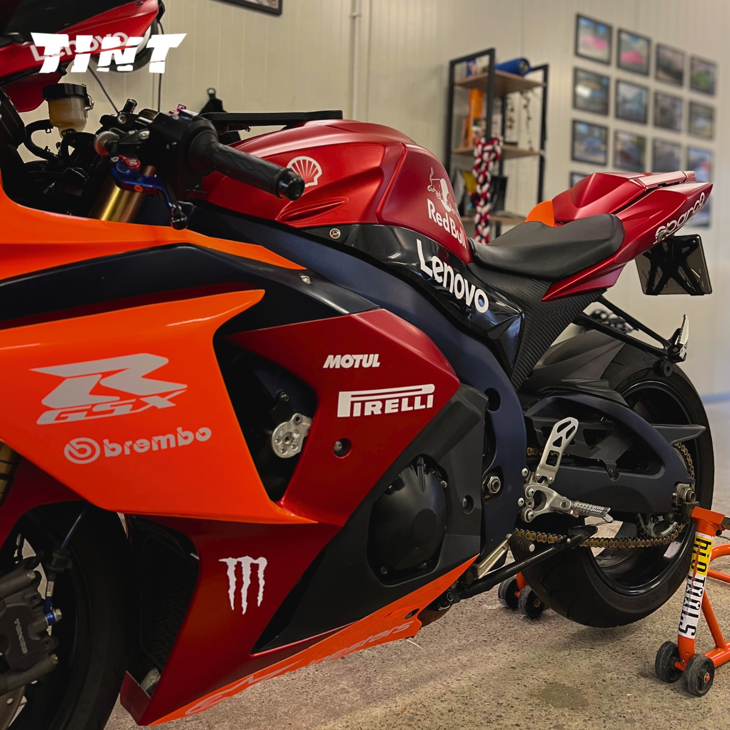 Sportowy motocykl w barwach wyścigowych z licznymi naklejkami sponsorów, stojący w garażu. Uwagę przykuwają detale oklejenia.