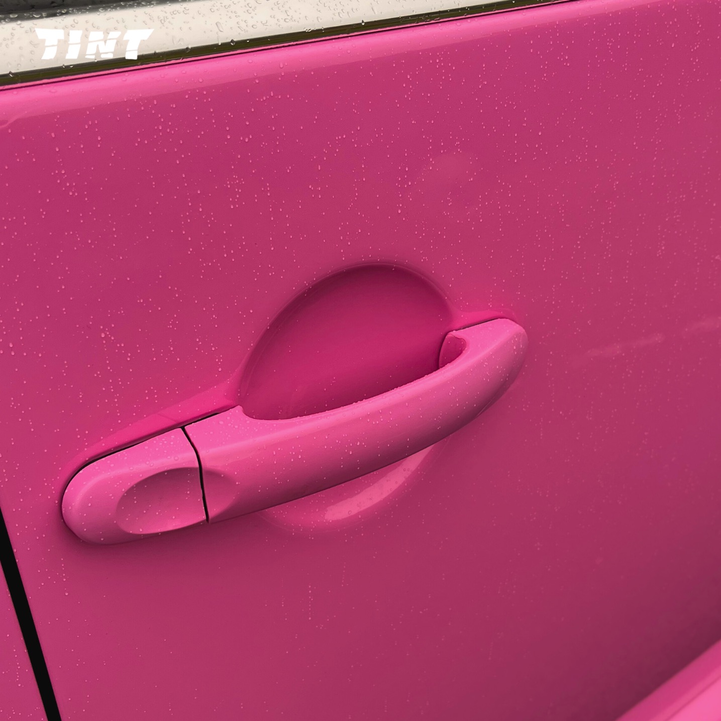 Różowy samochód po oklejeniu folią, widoczna klamka i krople wody. Intensywny kolor i gładka powierzchnia.