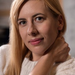 NO.TAK.STUDIO Natalia Olszewska - Portret uśmiechniętej blondynki w białym swetrze, z dłonią wspartą na szyi, w neutralnym oświetleniu.