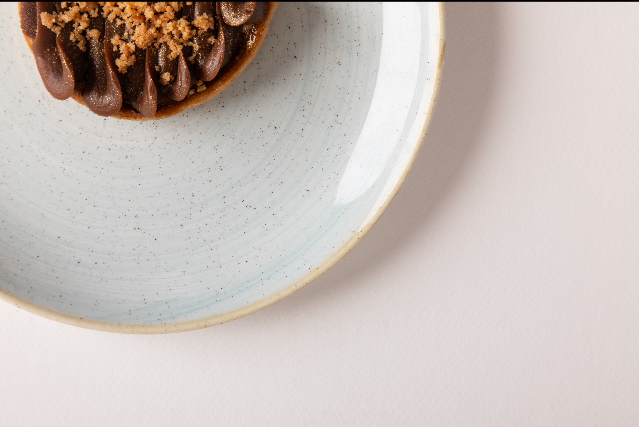 Tarta z kremem czekoladowym i posypką na talerzu z delikatnym niebieskim wzorem, ujęcie z góry, jasne tło.