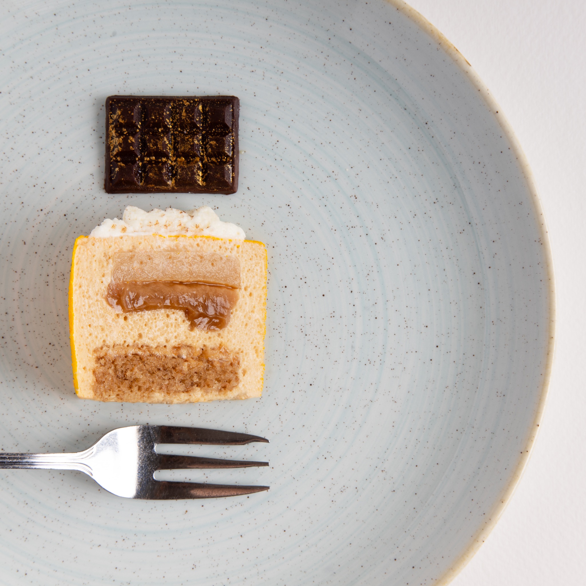 Przekrój ciasta z karmelem i czekoladką z jadalnym złotem, ułożone na talerzu obok widelca.