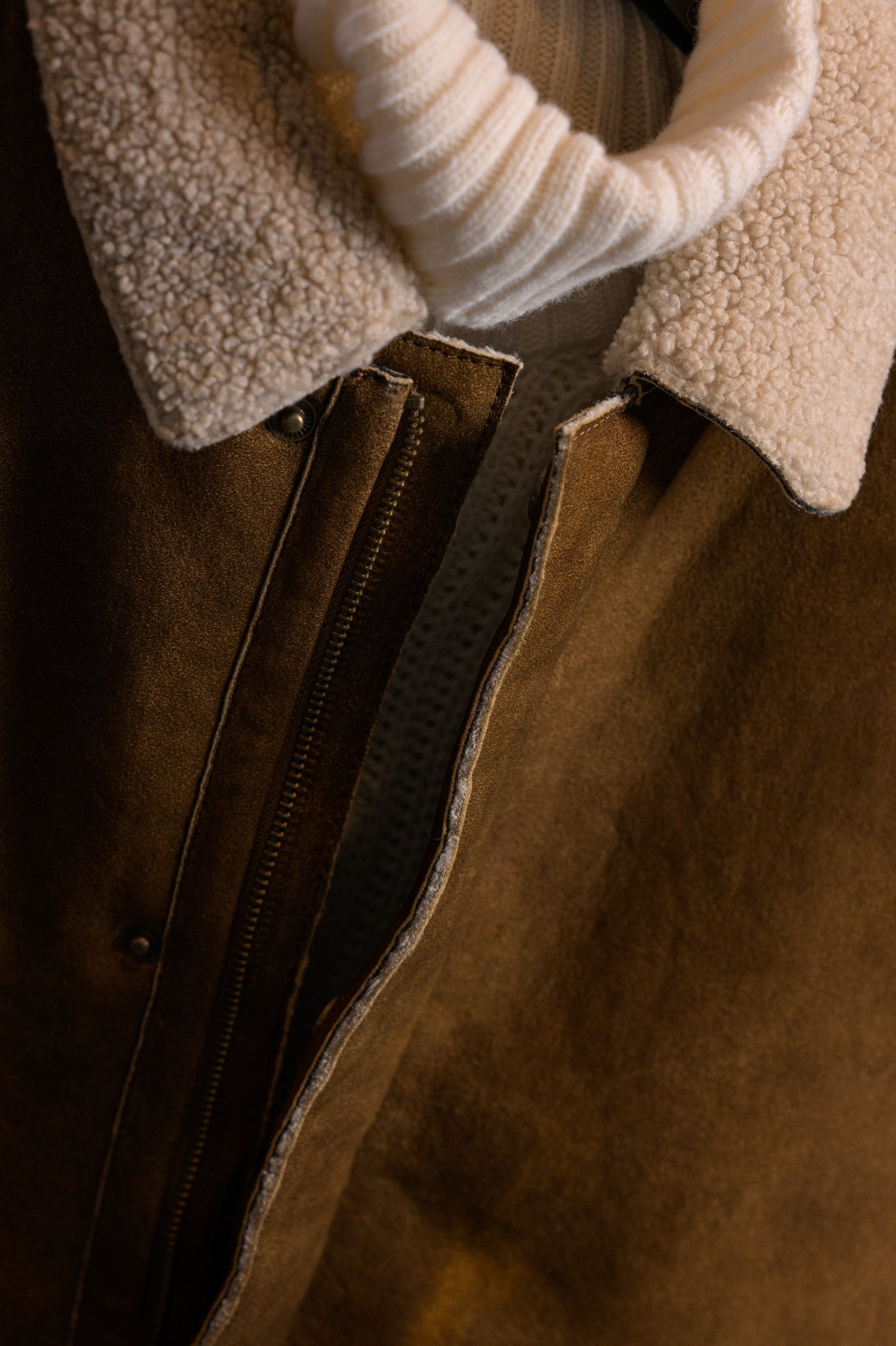 Brązowa kurtka z kożuchowym kołnierzem i kremowym golfem, widoczny zamek błyskawiczny i guzik.