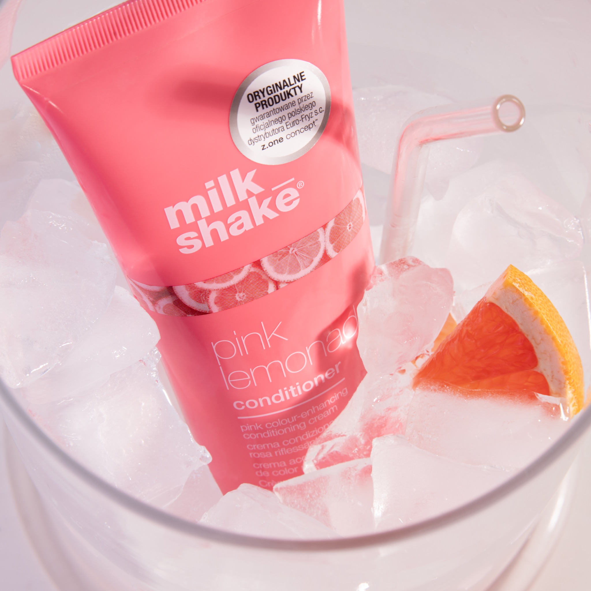 Różowa tuba odżywki do włosów Milk Shake Pink Lemonade zanurzona w kostkach lodu z plasterkiem grejpfruta i szklaną słomką, promocyjne ujęcie produktu.