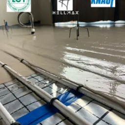 Wylewka anhydrytowa zalewająca rury ogrzewania podłogowego Henco, widoczne logo Knauf i Hellmax oraz certyfikat EC1