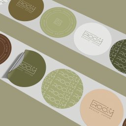 Maryna Slobodianiuk - Różnokolorowe okrągłe naklejki z logo 'ROOM beauty collab' w różnych wariantach kolorystycznych, ułożone na jasnym tle.