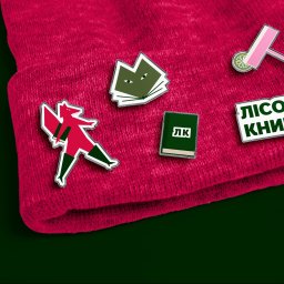 Maryna Slobodianiuk - Karmazynowa czapka z naszywkami: stylizowany lis, otwarte książki, samolot i napis 'LISOWA KNIHARNIA' na ciemnozielonym tle.