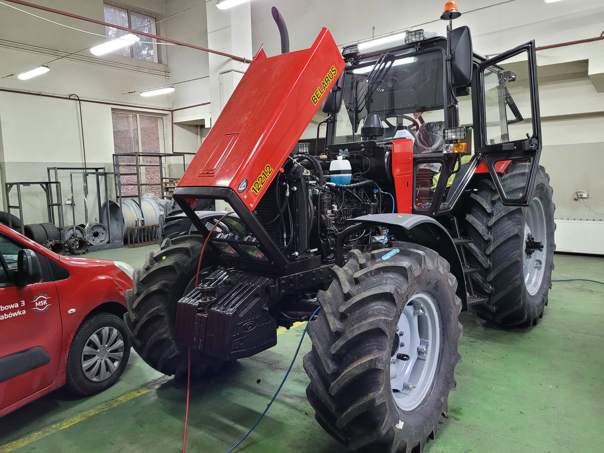 Czerwony traktor marki Belarus z otwartą maską silnika w warsztacie w Grabówce, widoczny fragment czerwonego samochodu z logo firmy.