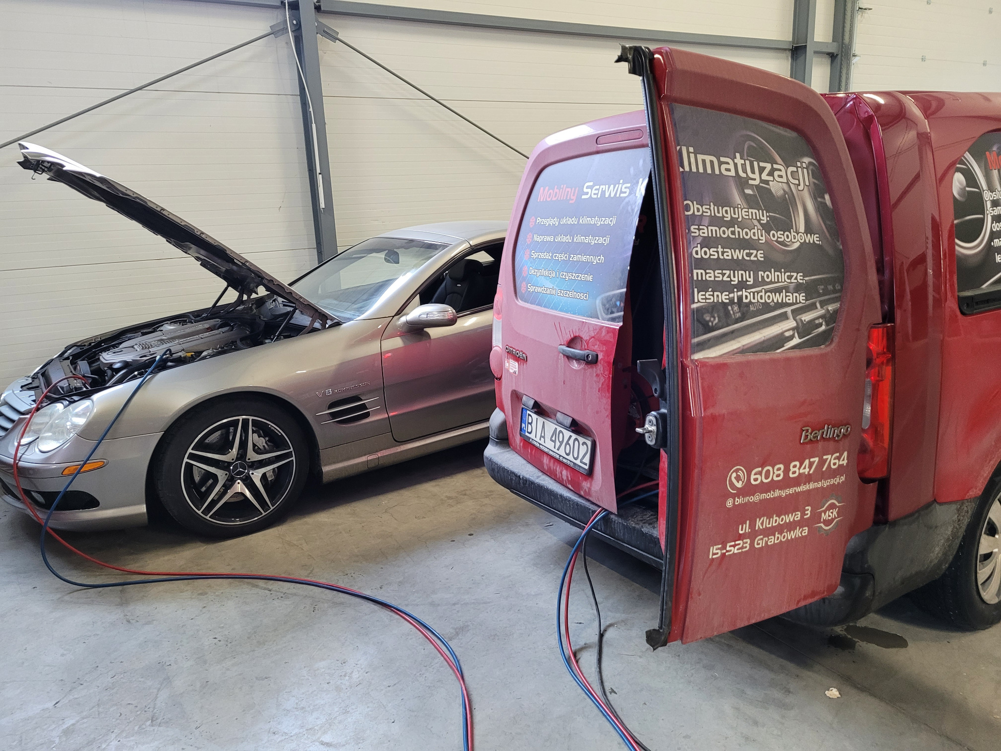 Srebrny Mercedes SL z otwartą maską podczas serwisu, obok czerwony Citroen Berlingo z reklamą mobilnego serwisu, widoczne przewody do obsługi układu chłodzenia.