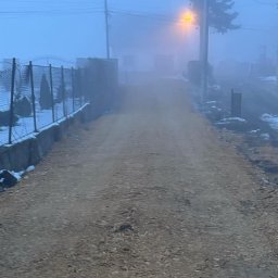 Posadzki żywiczne Podhale - Droga gruntowa po robotach ziemnych, widoczna w oddali zabudowa w gęstej mgle, częściowo ośnieżona, oświetlona lampą uliczną.