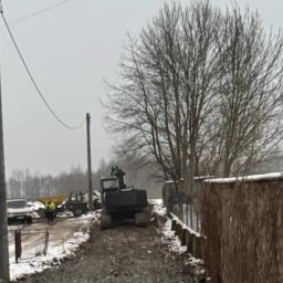 Posadzki żywiczne Podhale - Ciężki sprzęt budowlany ugniata kamienistą drogę w pochmurny dzień, z widocznymi przewodami elektrycznymi nad głową i fragmentami śniegu na poboczu.