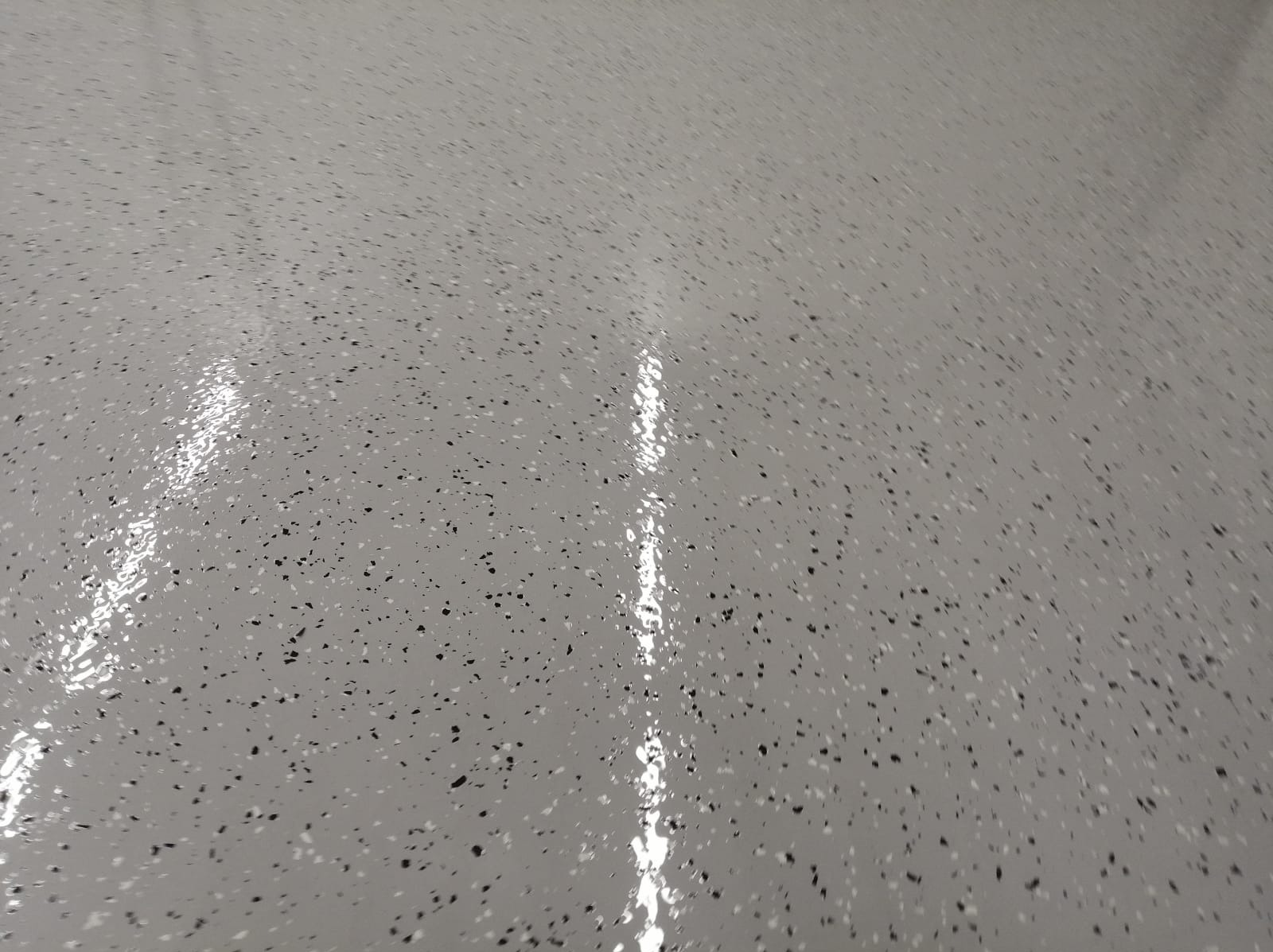 Jasnoszara, błyszcząca posadzka z drobnymi, czarnymi i białymi wtrąceniami, widoczne odbicie światła.