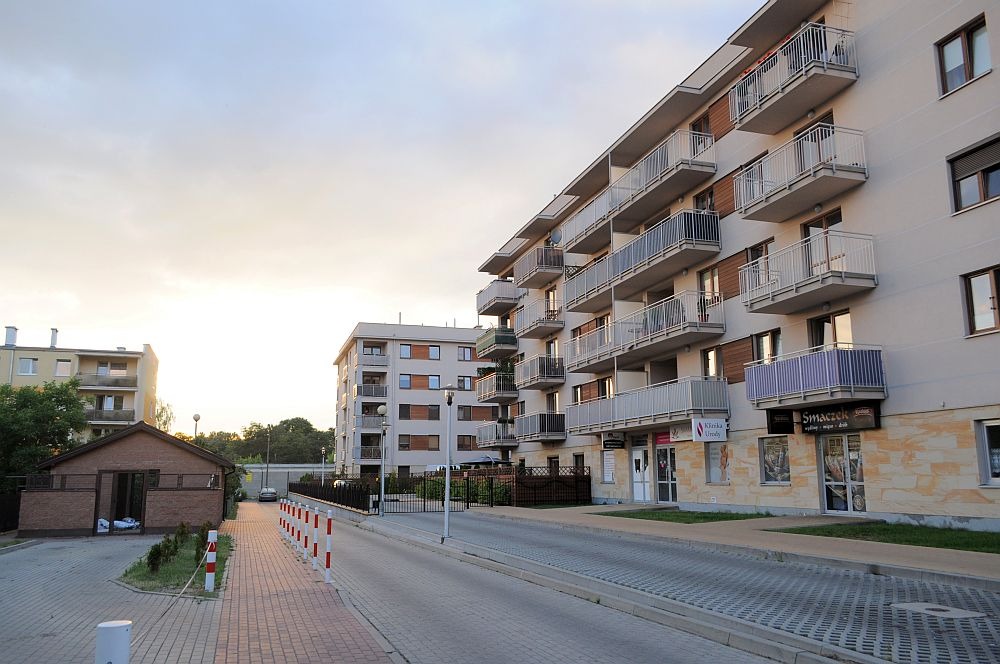Nowoczesne osiedle mieszkaniowe z balkonami i lokalami usługowymi na parterze, widoczne z poziomu ulicy.