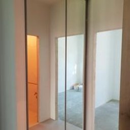 Rafal Sarnowski - Trzydrzwiowa szafa z lustrzanymi frontami w surowym wnętrzu, widoczne przejścia do innych pomieszczeń, ściany w stanie deweloperskim.