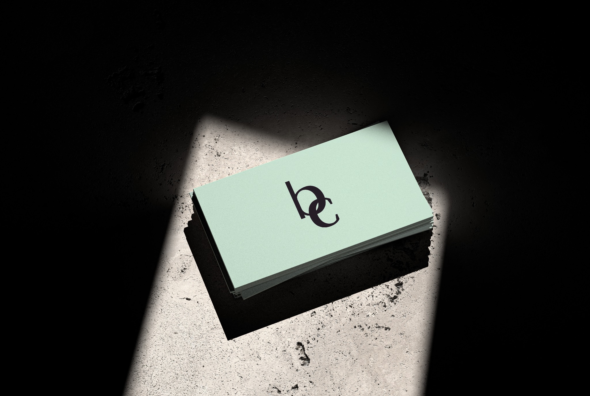 Stos wizytówek z minimalistycznym, czarnym logo 'bc' na jasnym, teksturowanym tle, oświetlony mocnym, kontrastowym światłem tworzącym dramatyczne cienie na szorstkiej powierzchni.