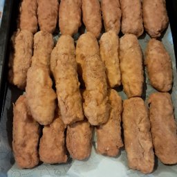 Katarzyna Wittbrodt - Rządki smażonych krokietów na blasze wyłożonej papierem do pieczenia. Domowy wyrób garmażeryjny z chrupiącą panierką w ciepłych odcieniach brązu.