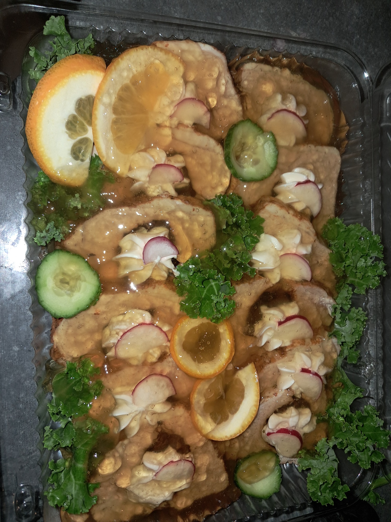 Gotowe danie w przezroczystym pojemniku: naleśniki polane sosem, udekorowane plasterkami rzodkiewki, ogórka, pomarańczy i zielonymi liśćmi sałaty.