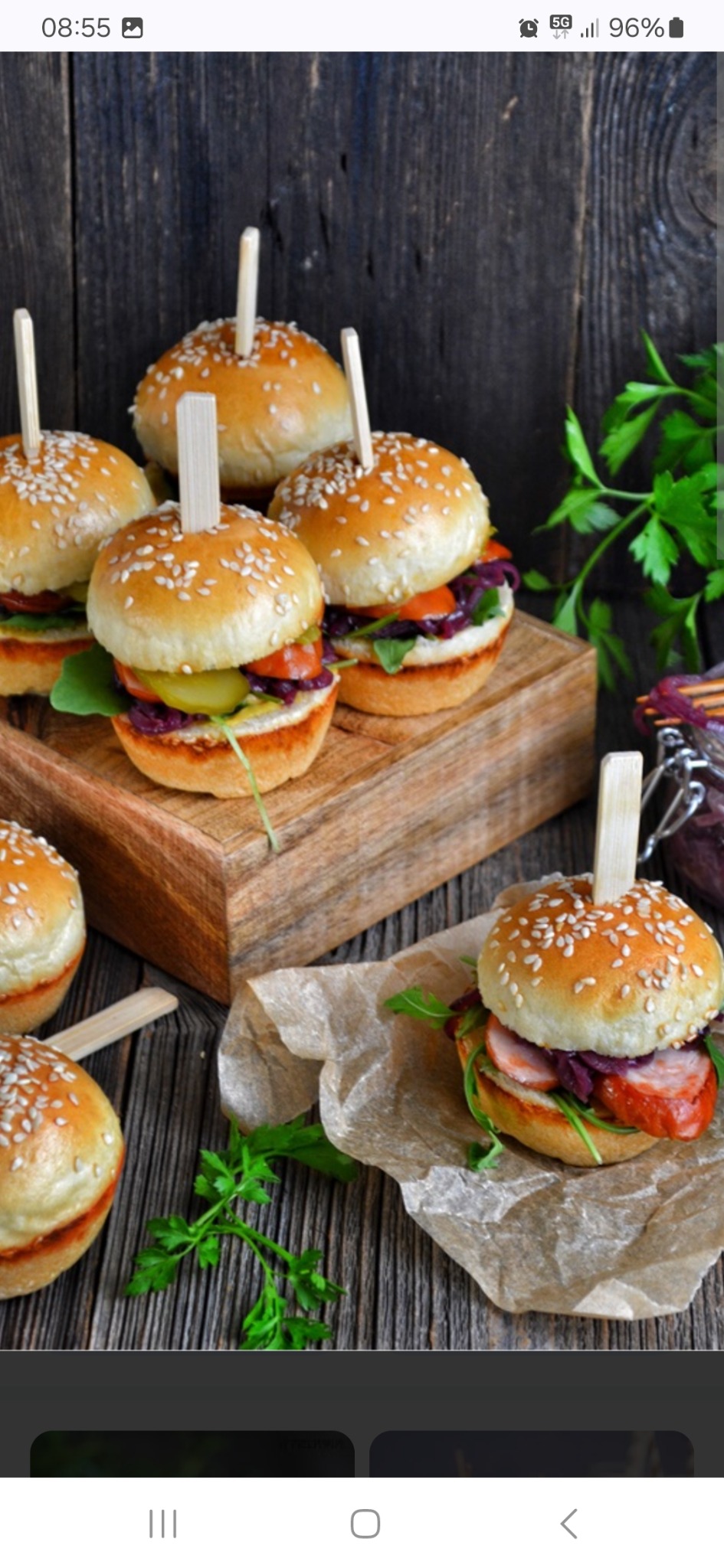 Mini burgery z sezamem, szaszłykami, czerwoną kapustą i rukolą, ułożone na drewnianej desce i papierze pergaminowym na tle rustykalnych desek.